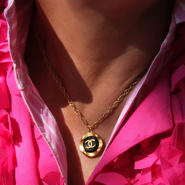 Złocony naszyjnik z guzikiem z logo Chanel na czarnym tle. BONJOUR MADAME